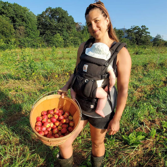 Allison with a baby in a carrier and a bushel of apples